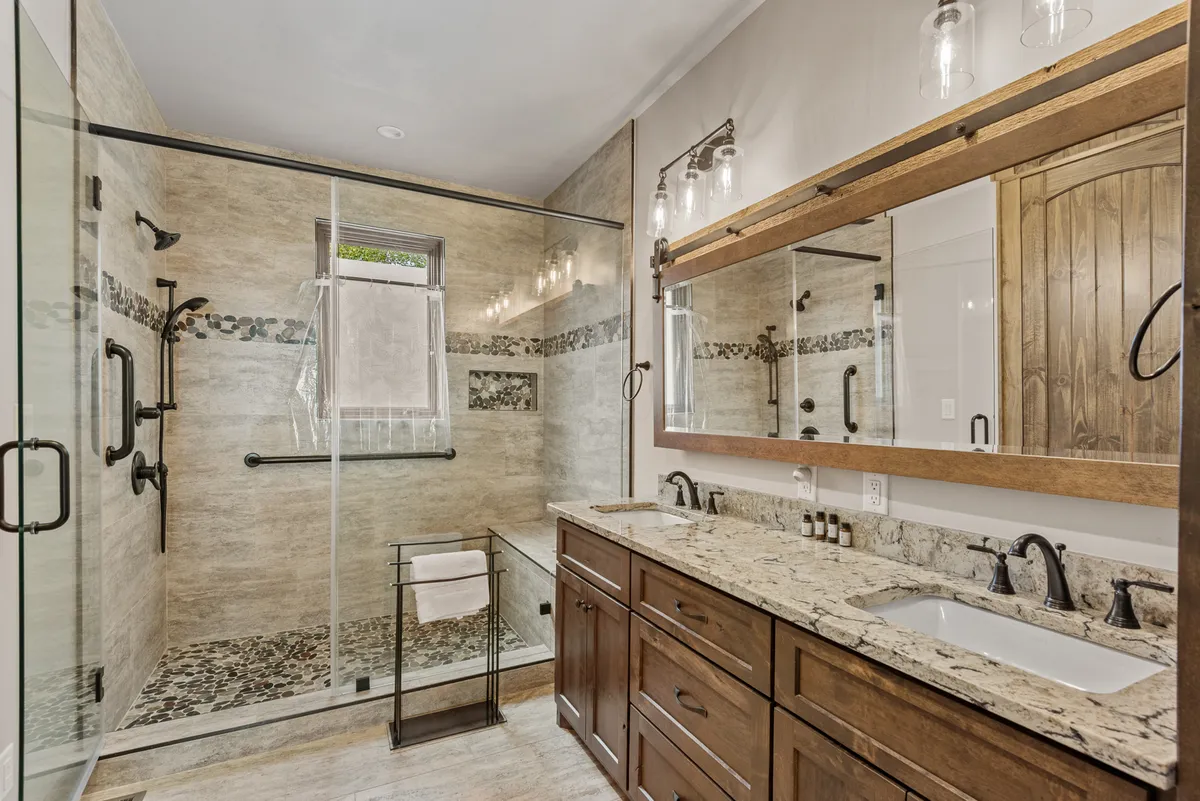 A spa-inspired bathroom with a glass shower enclosure, double vanity with natural stone countertops, and decorative tile accents. The layout and finishes evoke luxury and relaxation, perfect for a rejuvenating self-care routine.