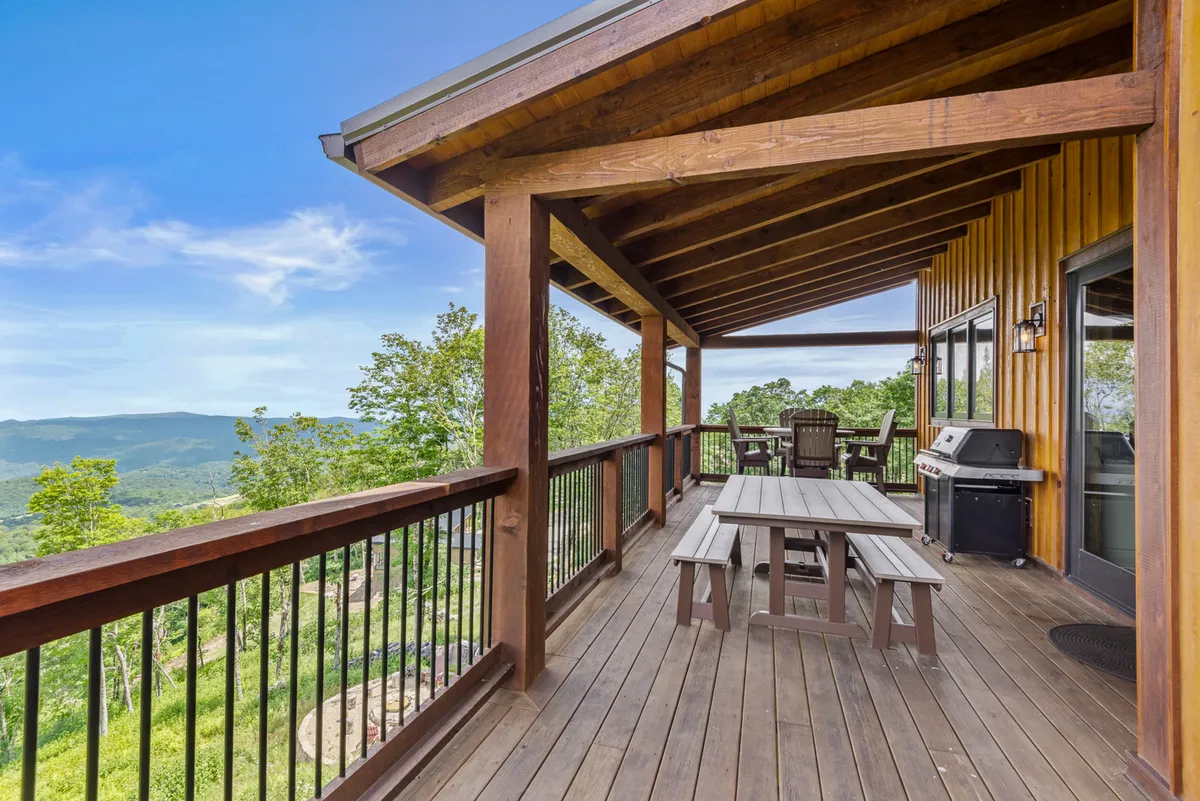 A spacious wooden deck furnished with outdoor seating and a grill, offering sweeping mountain views. The setting is ideal for alfresco dining or relaxing at sunset, with the serene landscape inviting guests to linger outdoors.