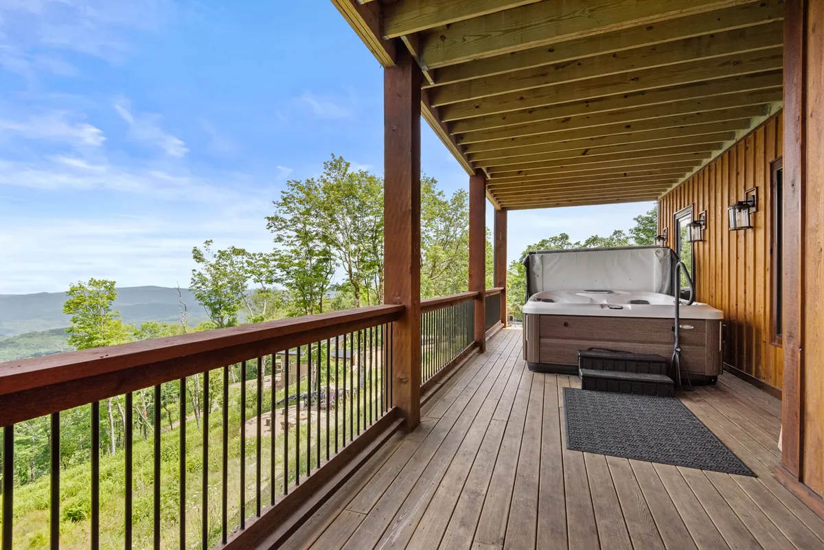 A luxurious hot tub sits on a wooden deck overlooking the mountains, surrounded by nature. The view from the deck stretches to the horizon, making it an inviting spot for relaxing after a day filled with mountain activities or for stargazing on clear nights.