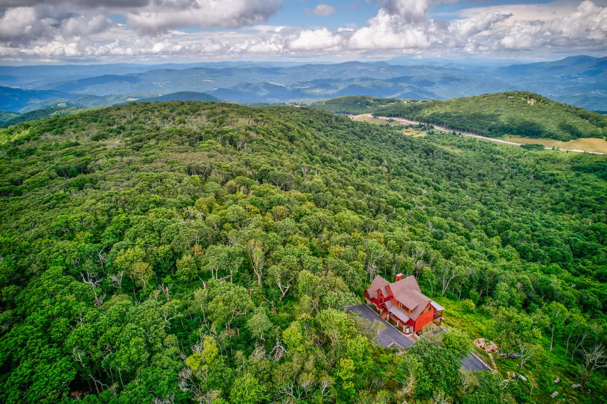 A striking view of the red house nestled among lush trees, with a sweeping mountain range in the background. The tranquil setting is ideal for outdoor activities such as hiking and nature walks, and the wide-open sky hints at stunning opportunities for stargazing or even glimpsing the Northern Lights.