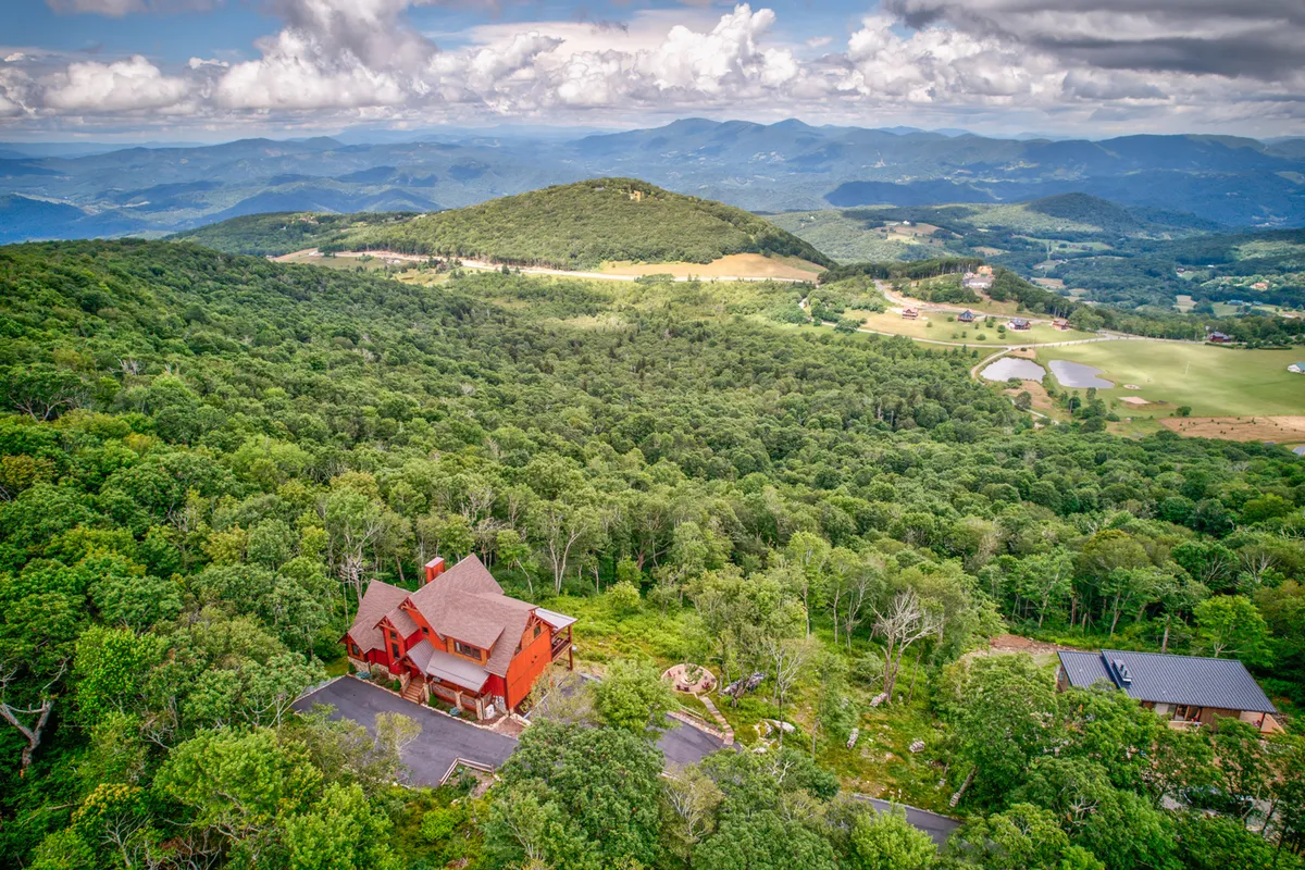 The red house stands amidst vibrant greenery, with the majestic mountains in the background. The tranquil setting invites guests to embark on hikes, observe wildlife, or simply enjoy the mountain air from the balcony.