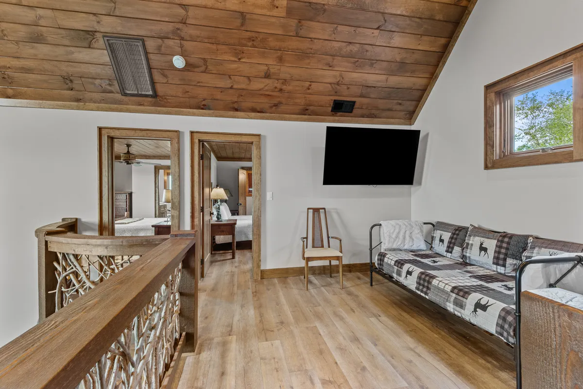 A comfortable sitting area featuring a plaid-patterned sofa, wooden railing, flat-screen TV, and open doorways leading to other parts of the home. The layout is ideal for family movie nights, board games, or simply enjoying quiet moments together.