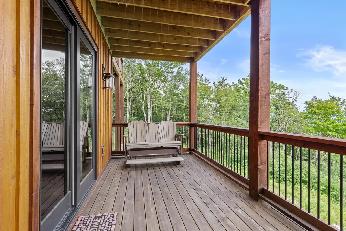 A peaceful deck lined with classic wooden rocking chairs, surrounded by lush trees and a sturdy railing. The scene invites guests to relax, read, or sip a drink while taking in the natural beauty and sounds of the mountains. The ambiance is intimate and inviting, perfect for couples.